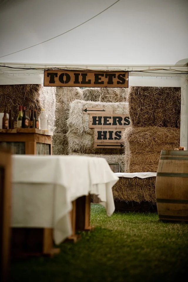 Sign indicating a men's and women's bathroom at an outdoor event with hay bales in the background.