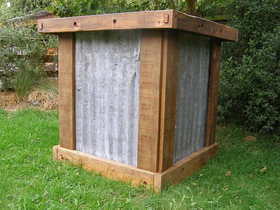 Wood and metal outdoor compost bin in a garden.
