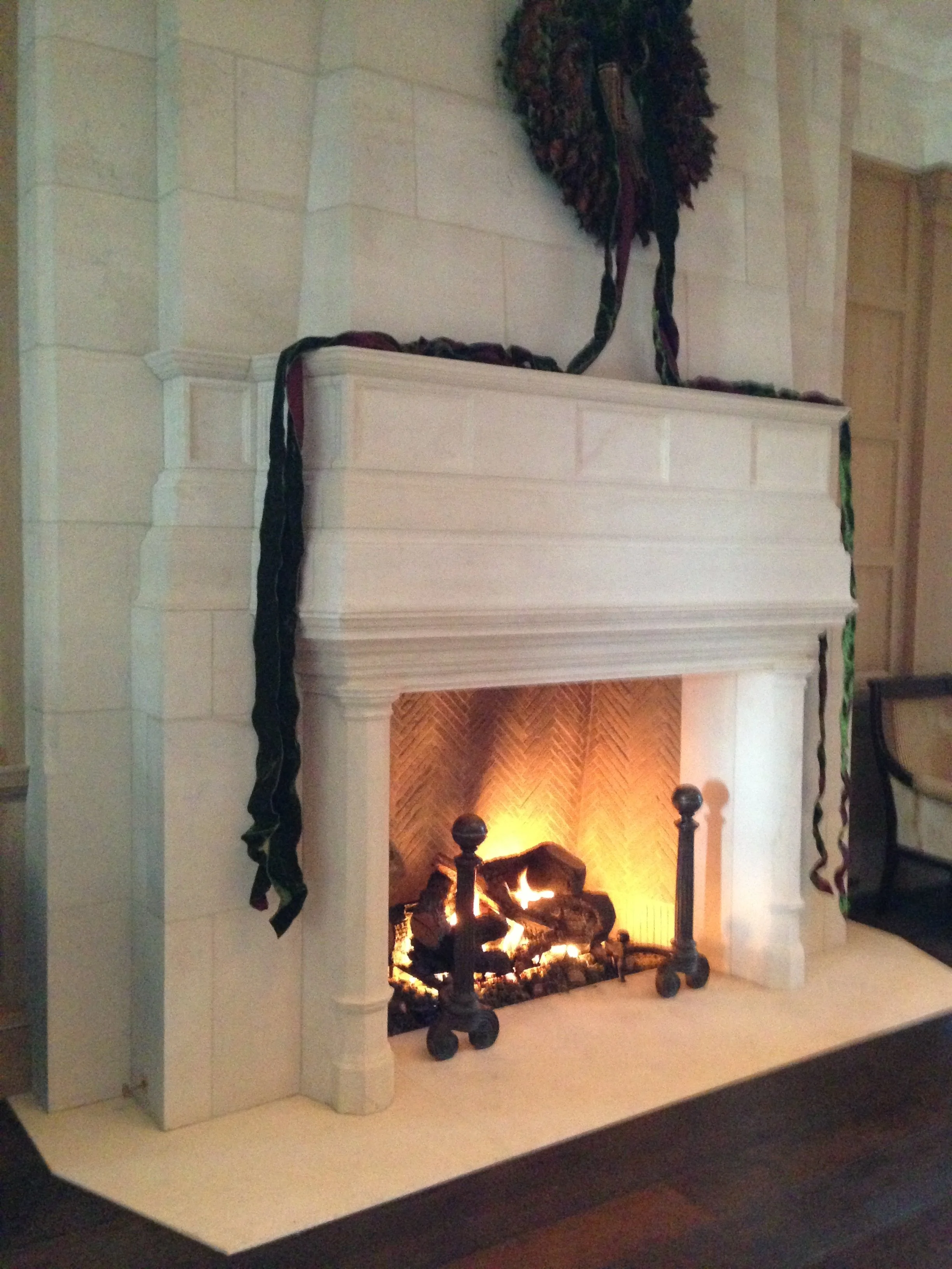 A white stone fireplace with a fire burning inside, decorated with black and green ribbons draped over the mantel and sides.