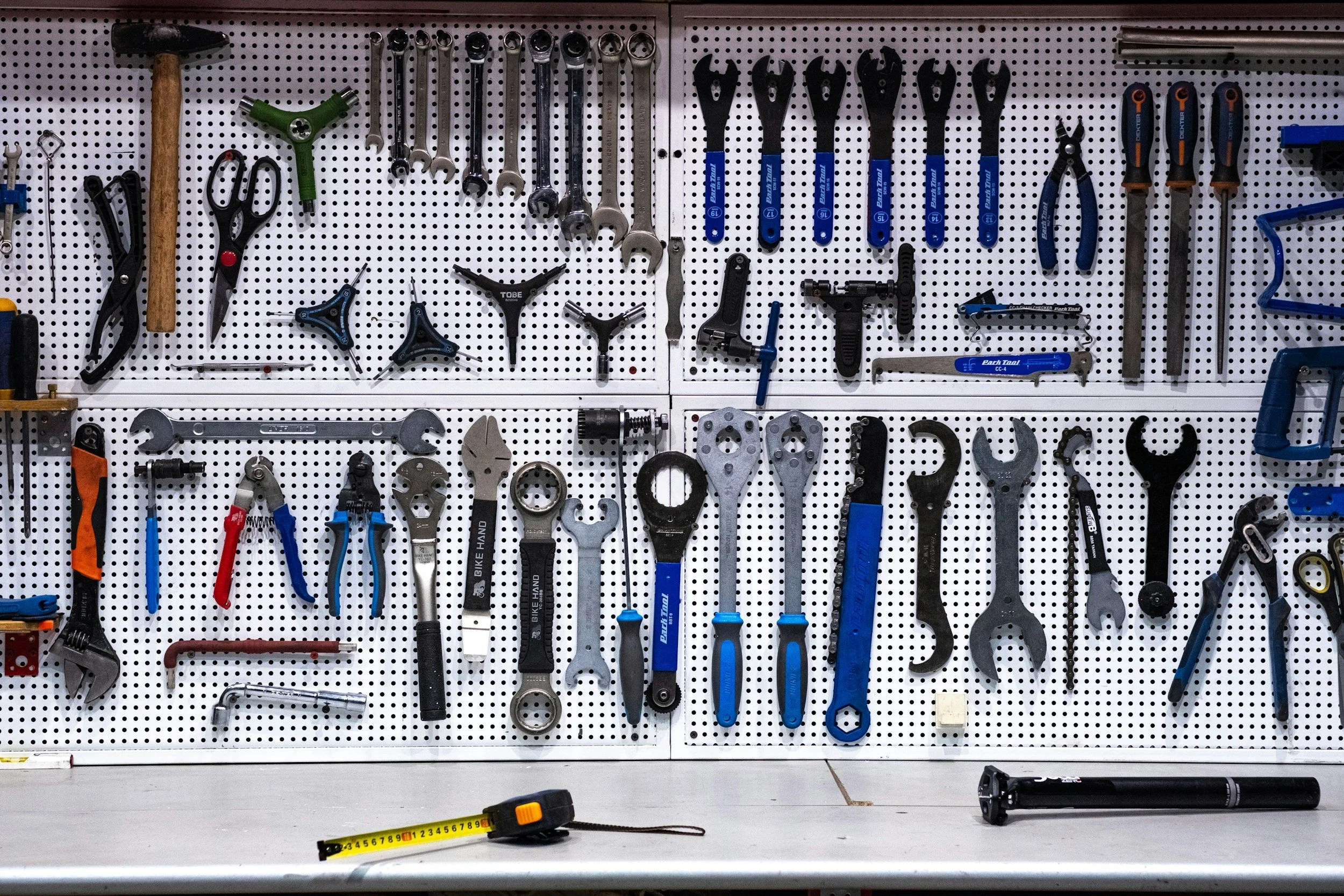 Tools organized on a pegboard, including wrenches, screwdrivers, pliers, and other hand tools, with a measuring tape and a bike pump on the work surface.