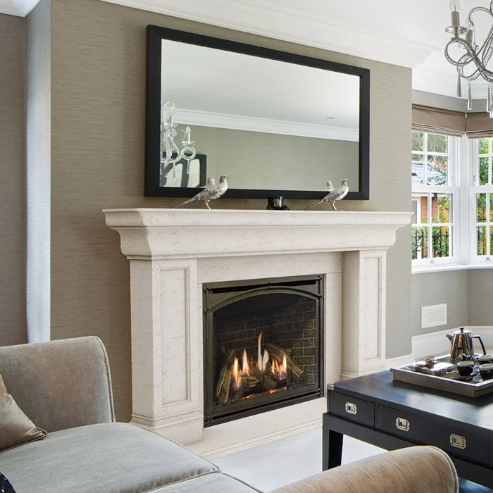 Living room with fireplace, mirror above it, two silver bird figurines on mantel, beige sofa, black coffee table with tray, window with beige curtain, chandelier.