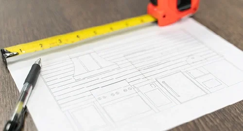 Blueprint of a building layout on a table with a measuring tape and pen nearby.