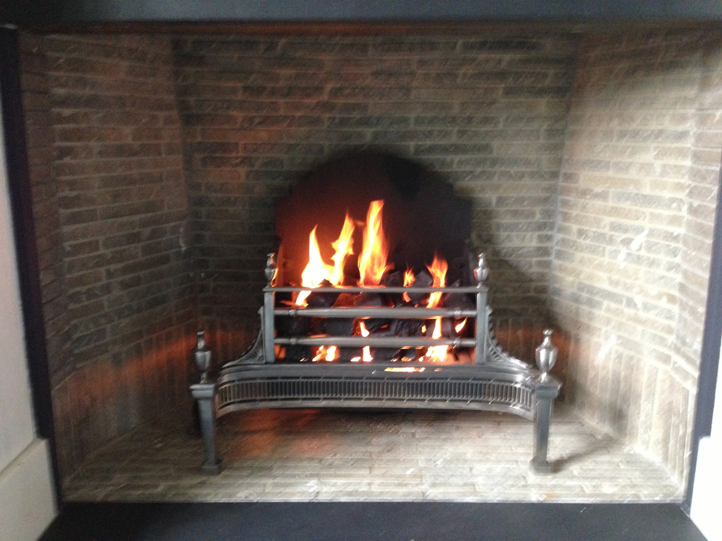 Fire burning in a brick fireplace with a metal grate and decorative metal posts on each side.