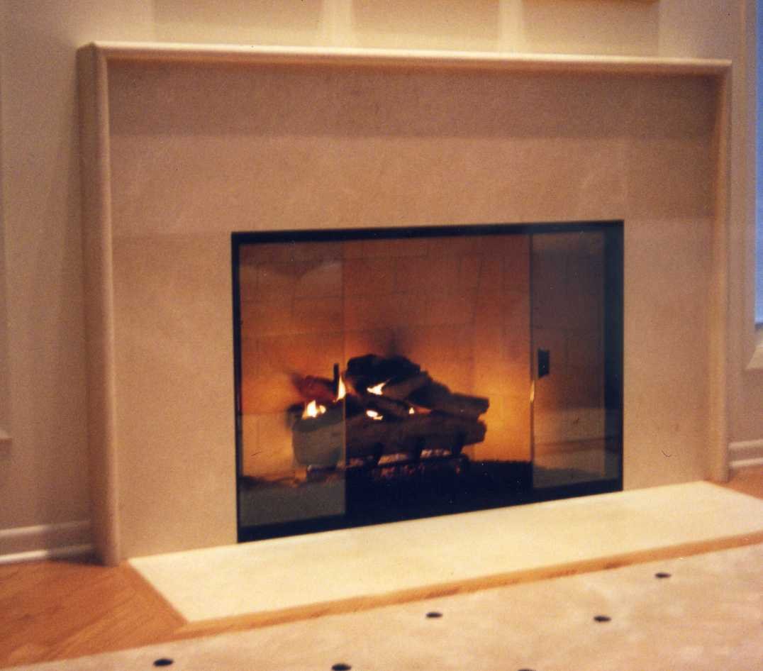 A modern fireplace with a glass front and a beige surround, with a fire burning inside.