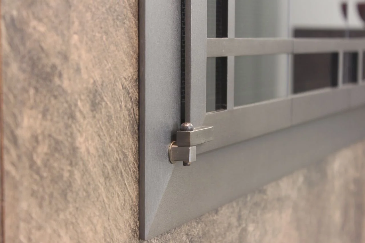 Close-up of a metal window security grille attached to a concrete wall.
