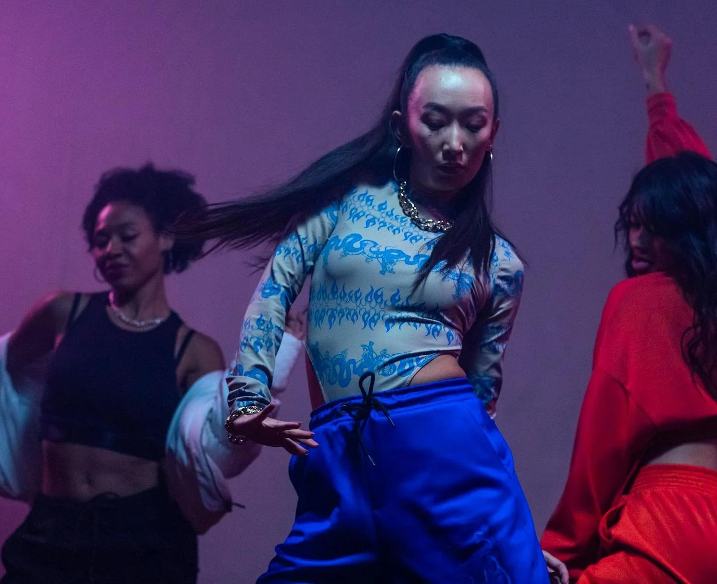 Asian woman with long black hair looking down while dancing wearing bright blue outfit