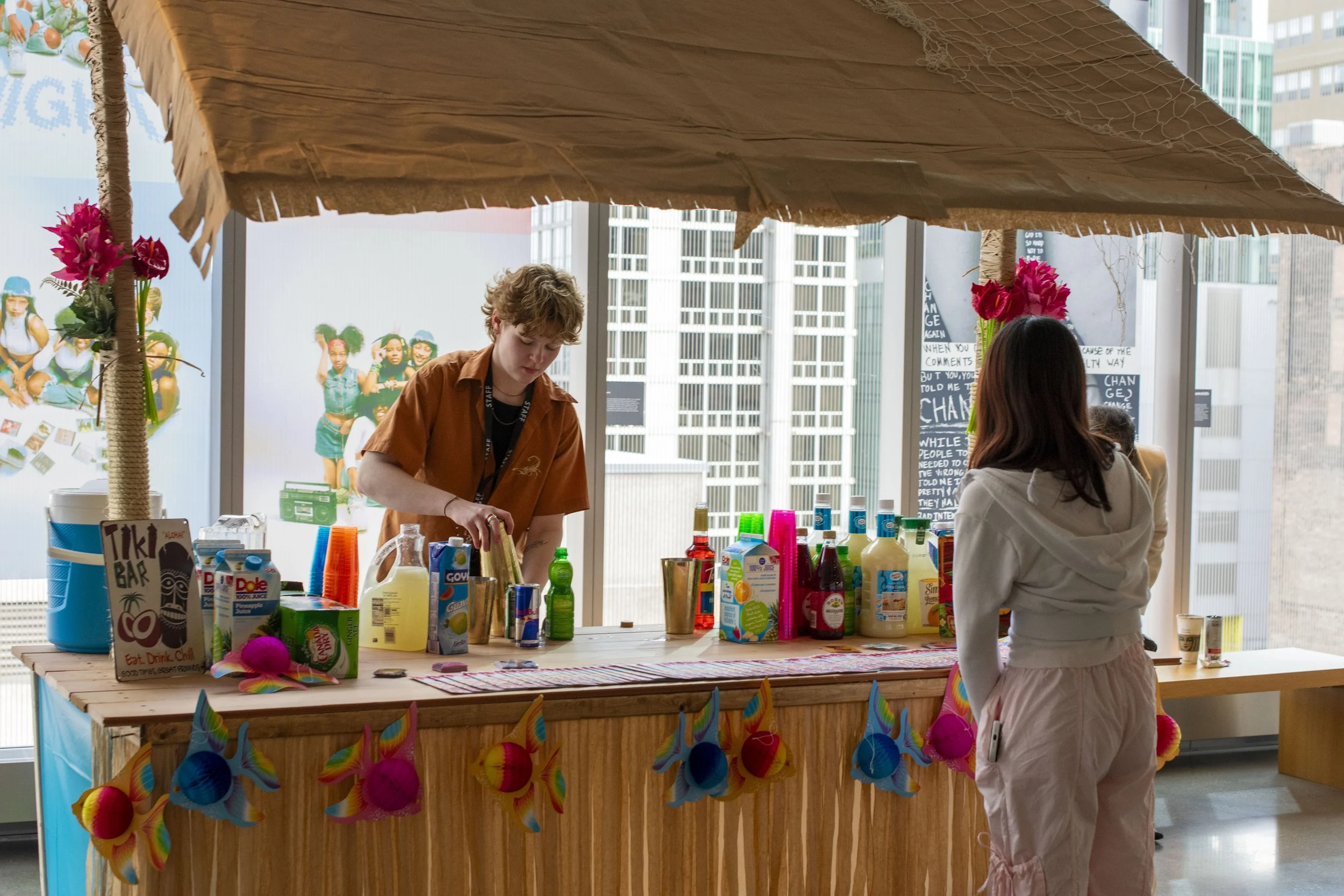 A person making drinks at a tiki bar setup with colorful decorations in a city indoor space.