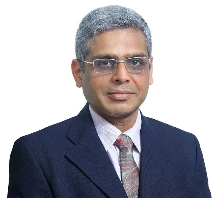 A professional man with gray hair and glasses wearing a dark suit, white shirt, and paisley tie against a white background.