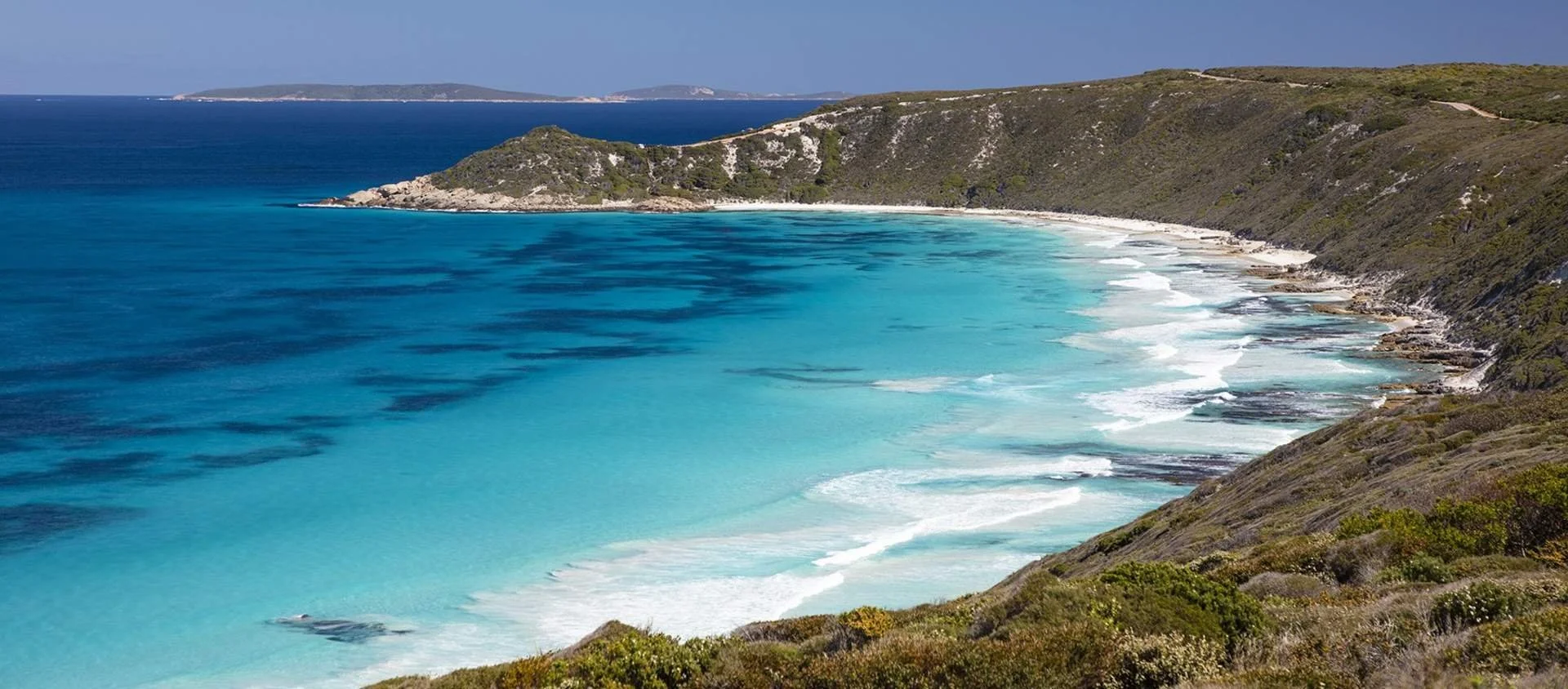 Scenic view of a beach with turquoise water and green hills surrounding it.