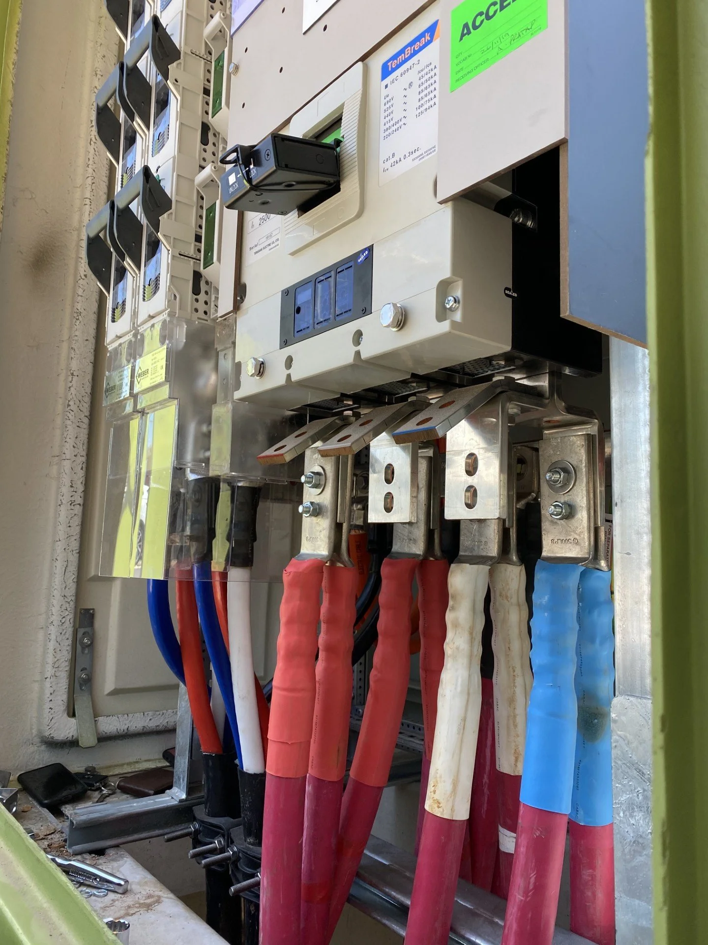 Electrical control panel with colored cables connected to metal terminals, switches, and a small digital device mounted on a white box.