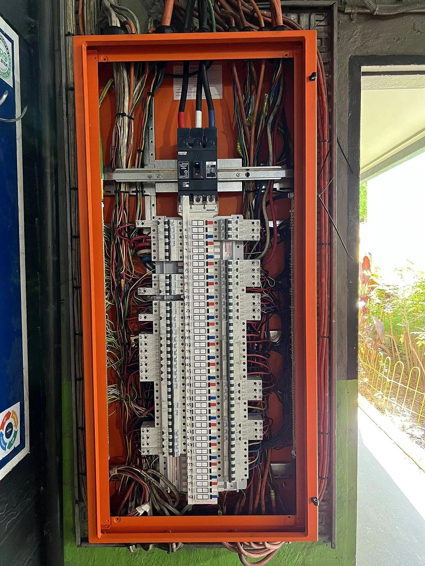 Electrical control panel with wires, circuit breakers, and switches inside an orange metal box.