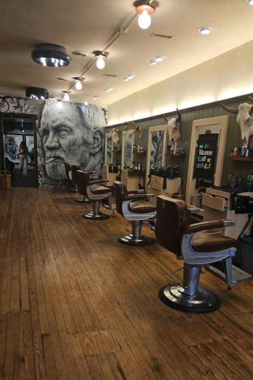 Empty barber shop with four vintage-style barber chairs and a mural of an elderly man's face on the wall.