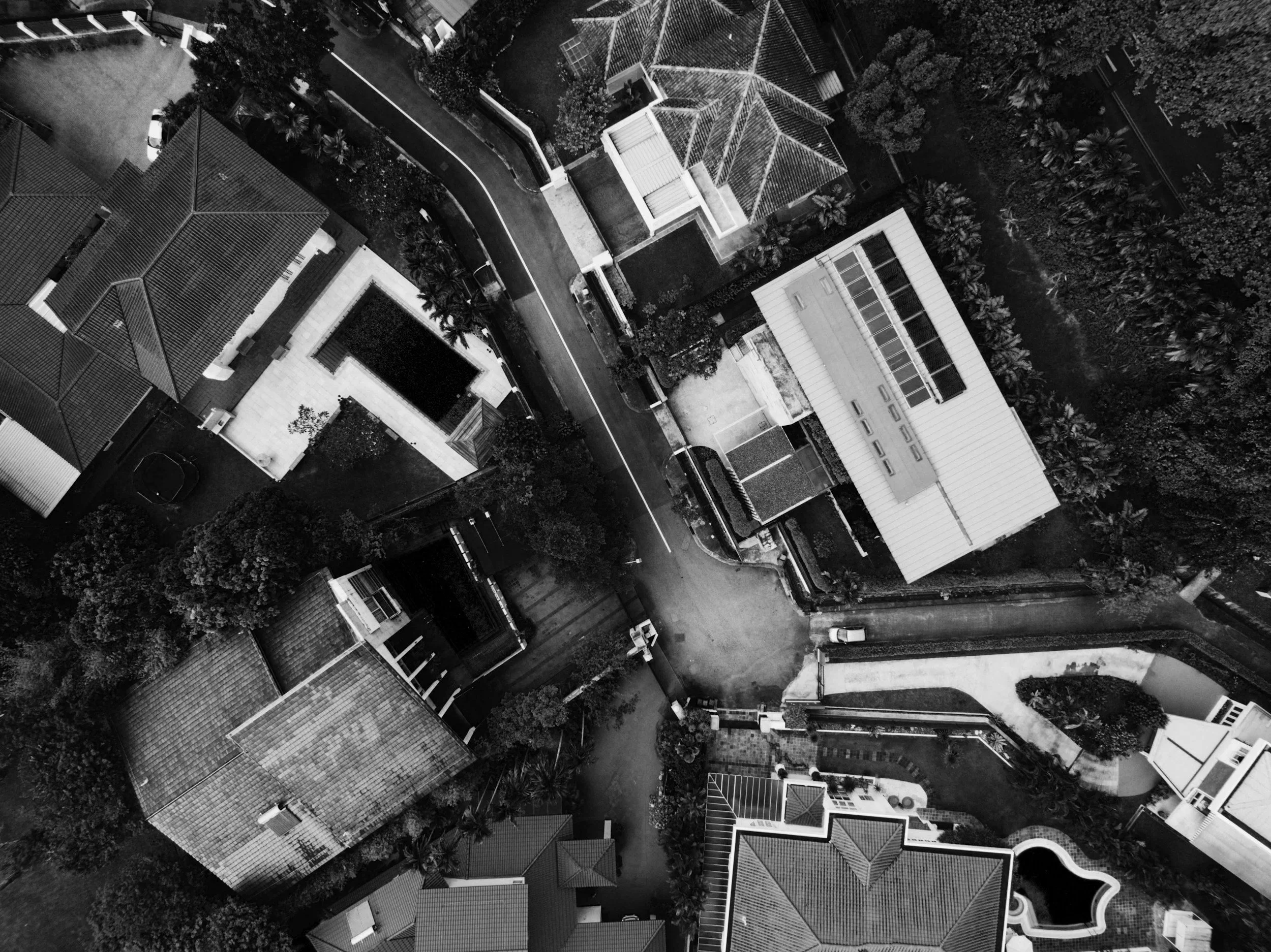 An aerial black and white photo of a residential neighborhood showing several houses with tiled roofs, a curved street, trees, and driveways.