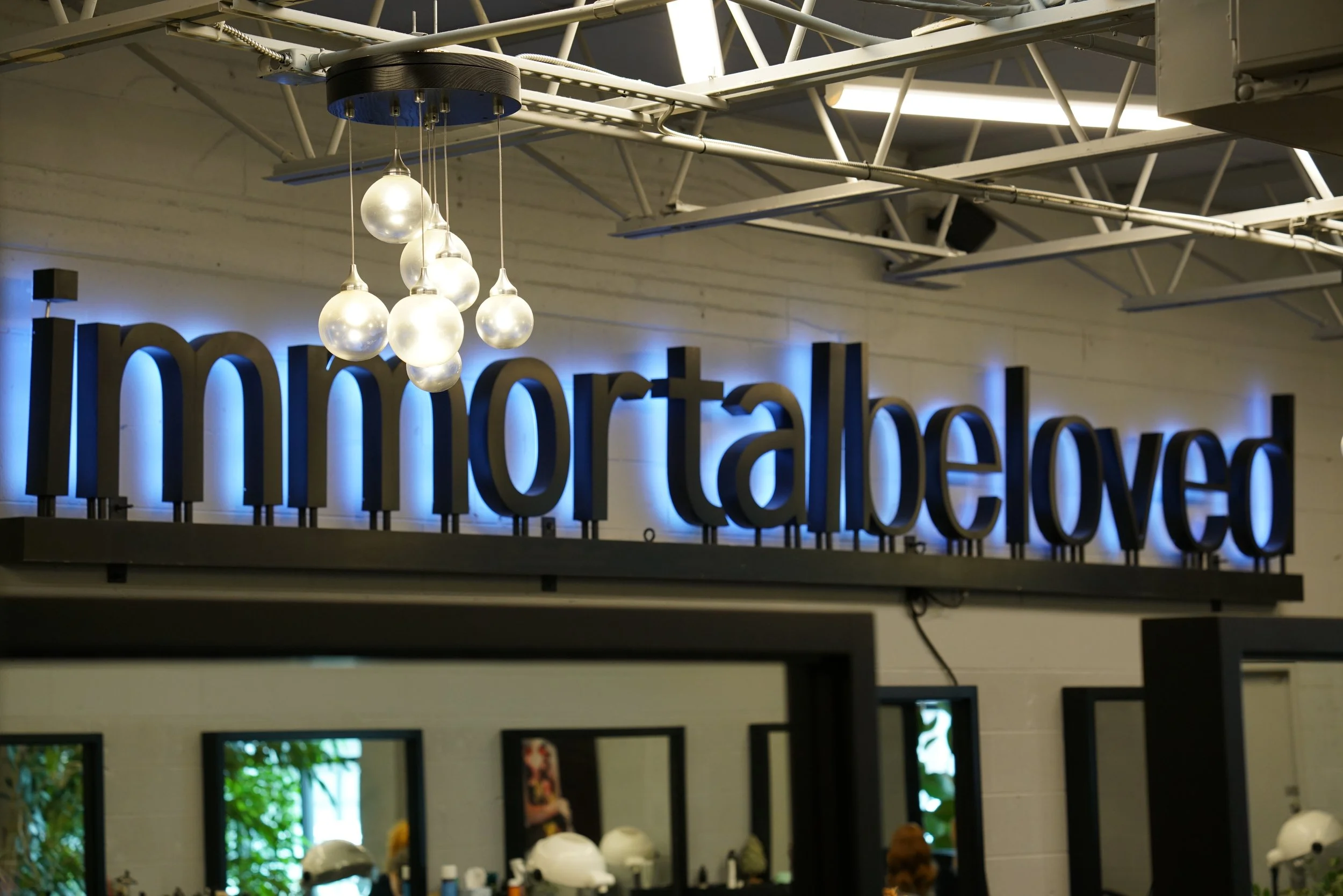 Sign reading 'immortabello' inside a restaurant or café, with hanging light fixtures and large mirrors in the background.