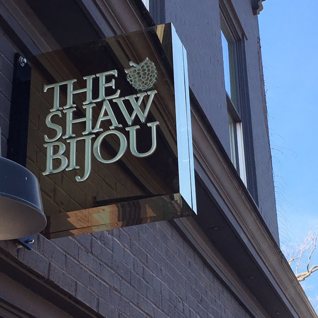 Business sign for "The Shaw BIJOU" with a graphic of a raspberry, mounted on the exterior brick wall of a building.