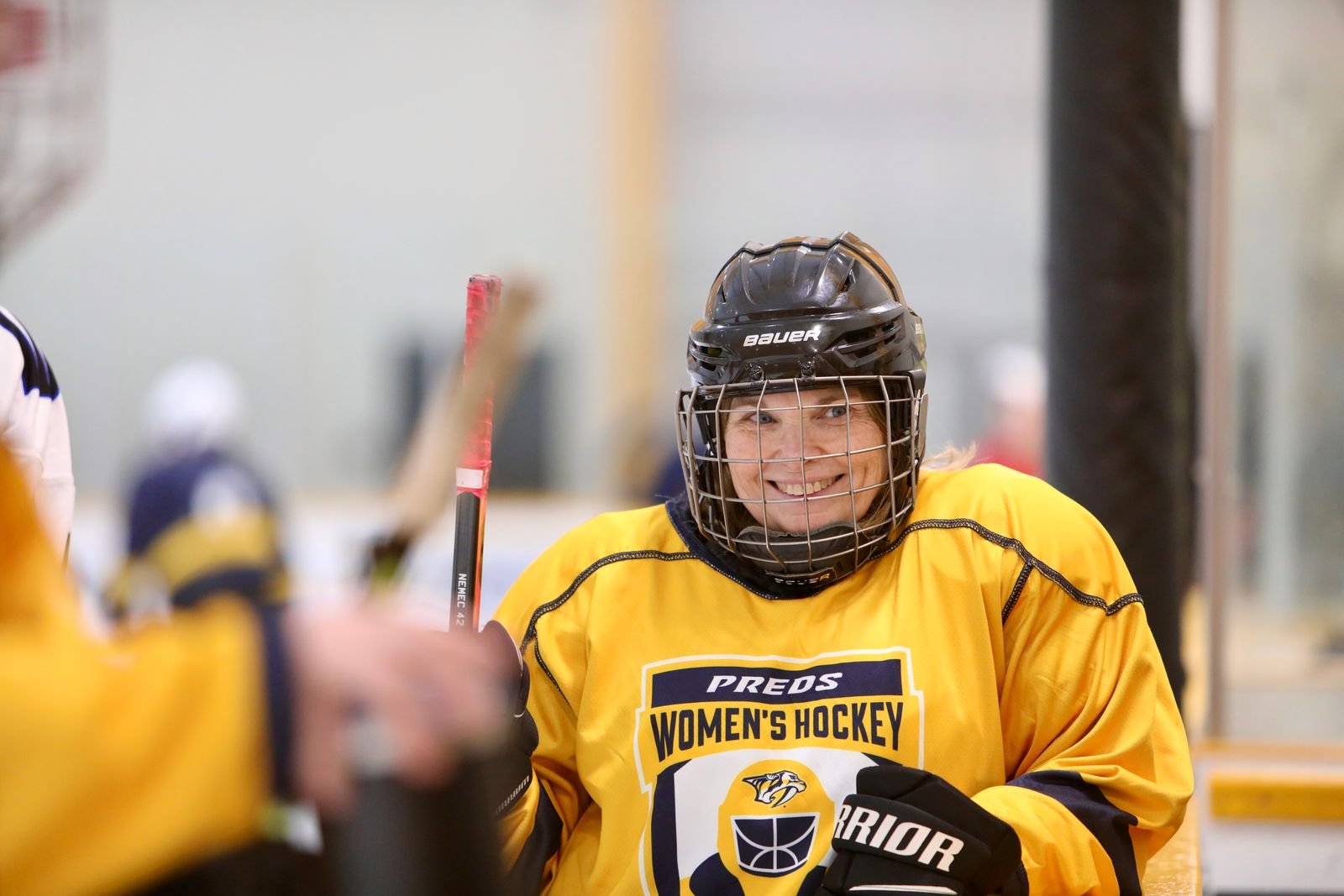 A woman in a yellow women's hockey jersey and black helmet smiling at the ice rink.