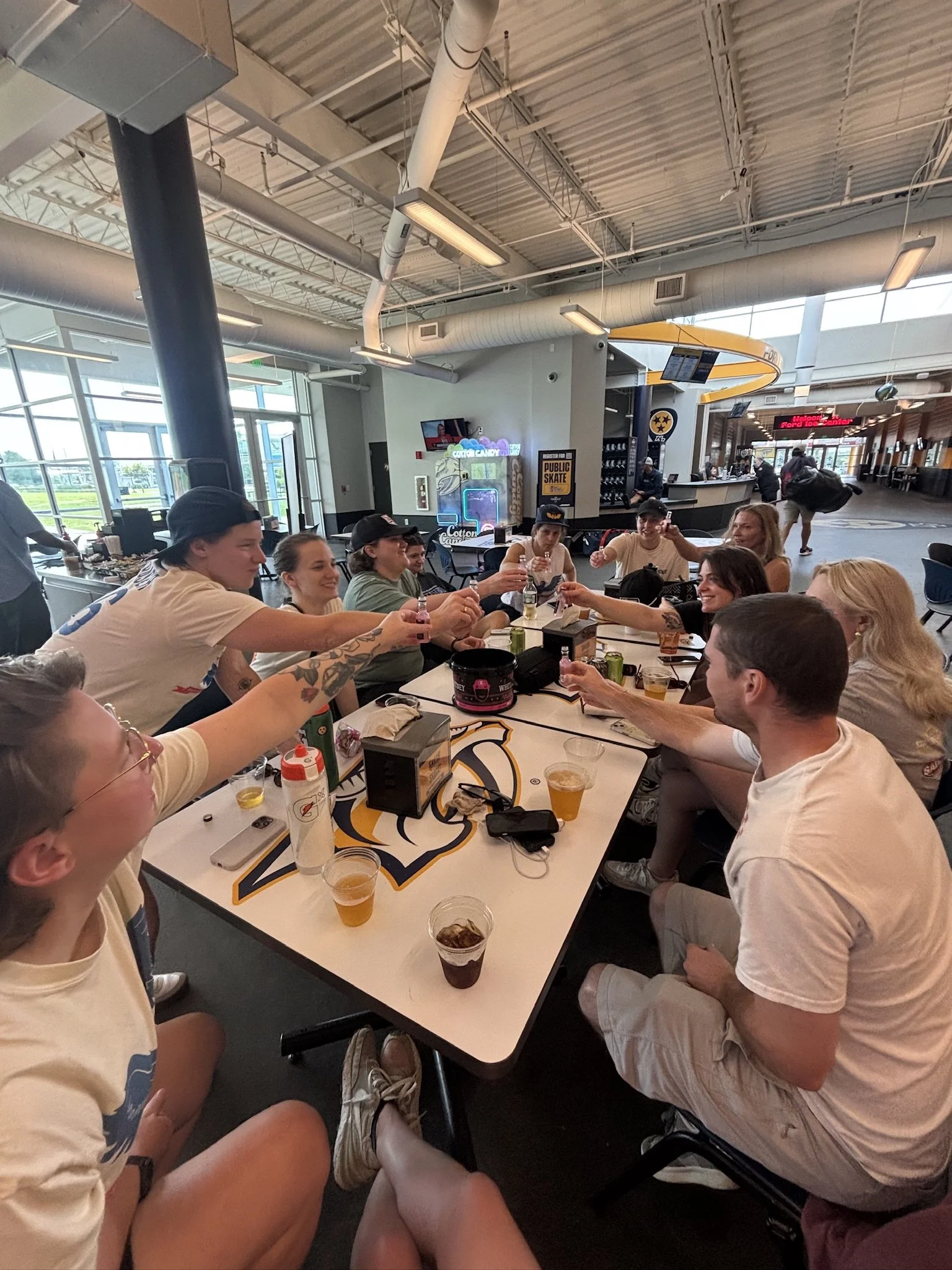 A group of people sitting around a table at a casual indoor dining area, raising their glasses for a toast.
