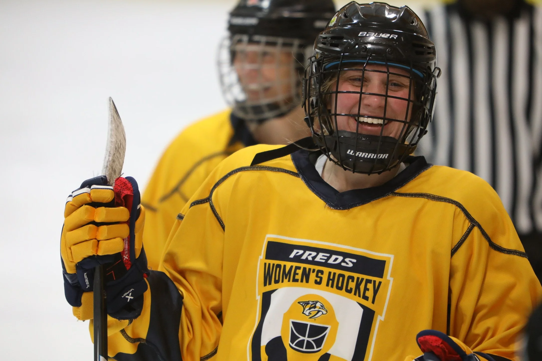 Women hockey players in yellow jerseys celebrating on the ice, smiling, and wearing black helmets.