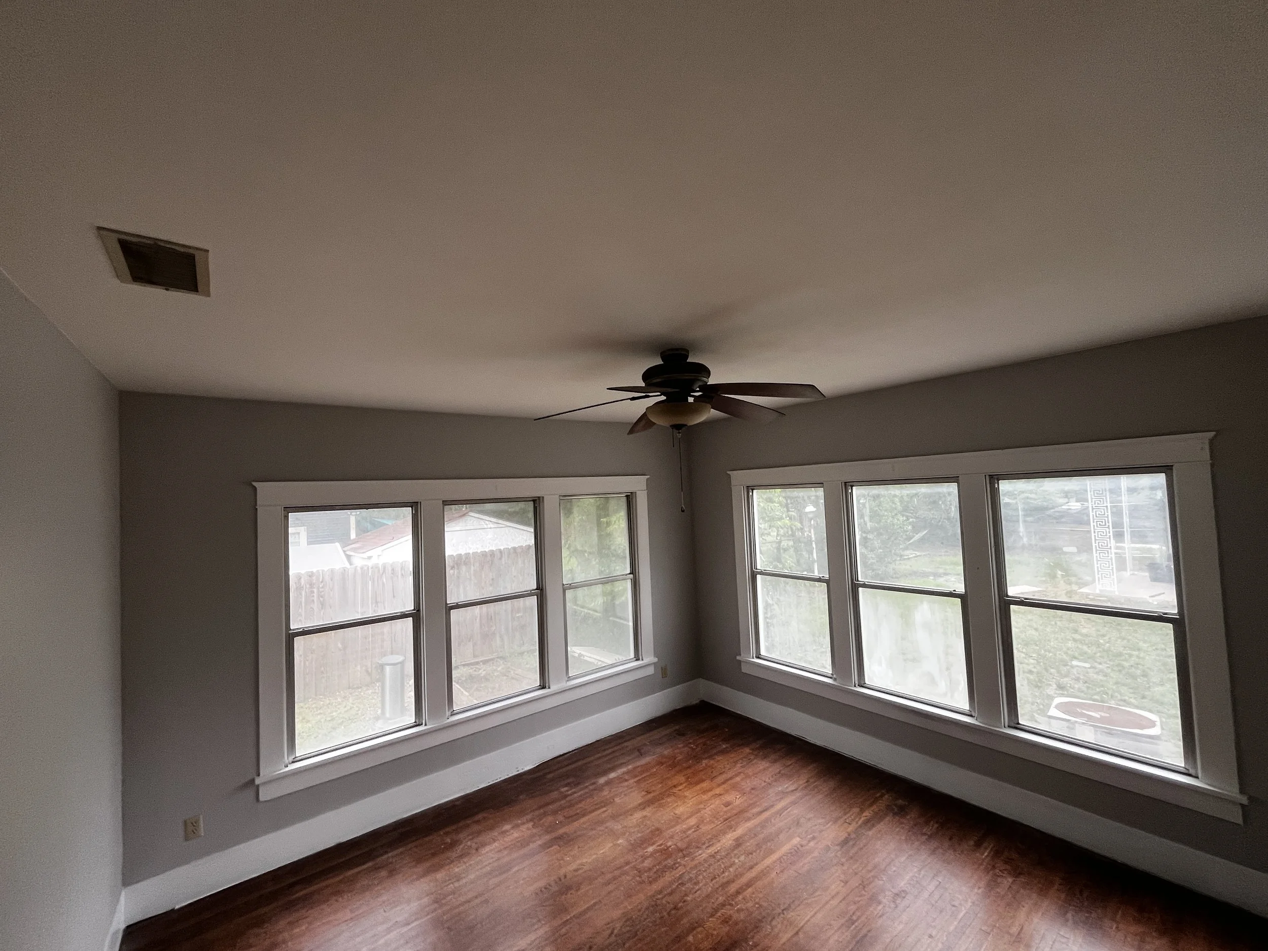 Living room with large windows, ceiling fan, hardwood floors, and gray walls