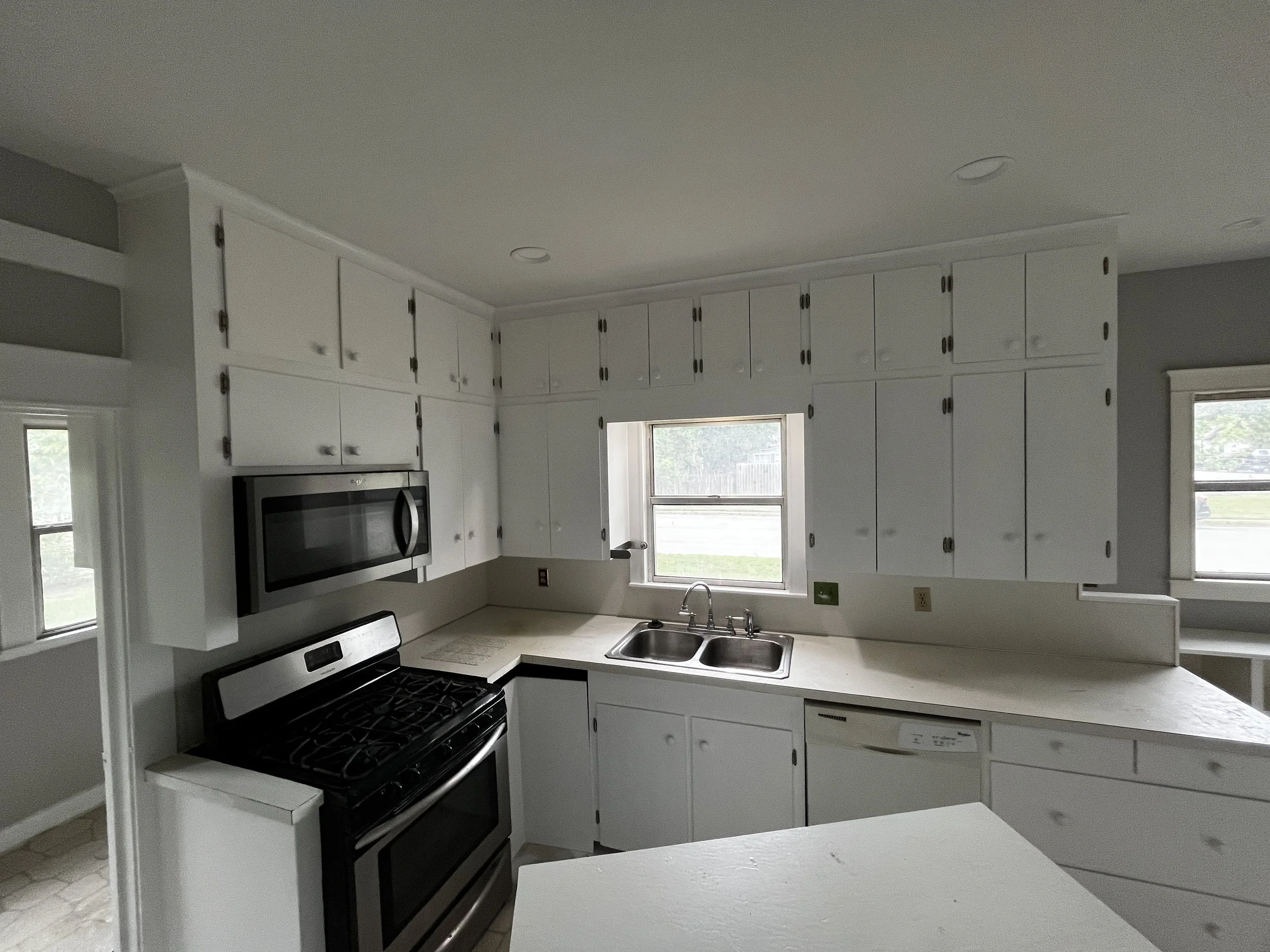 Kitchen with white cabinets, black stove, stainless steel microwave, and a double sink under a window.
