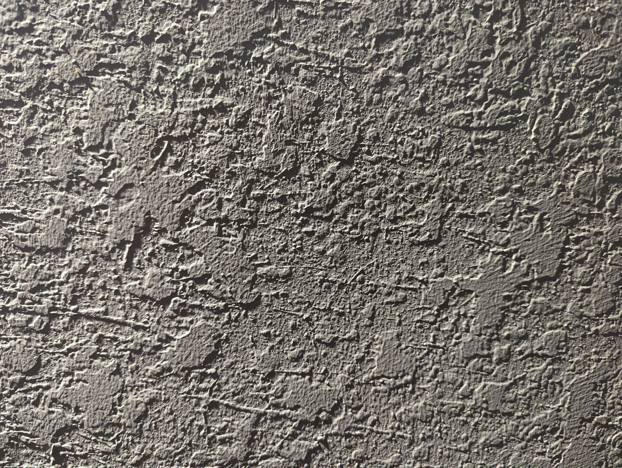 Close-up view of a textured concrete wall surface with rough, uneven pattern.
