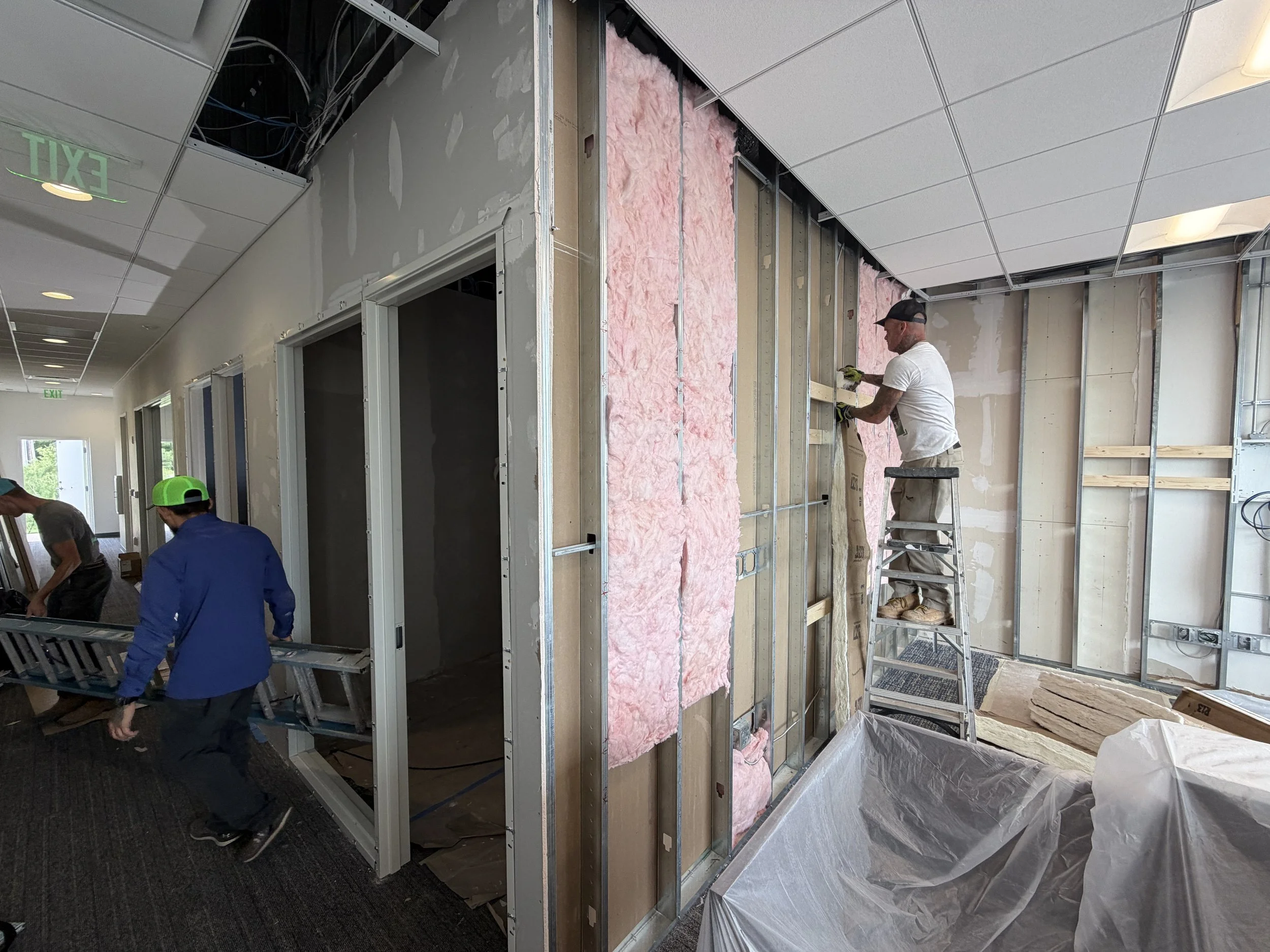 Construction workers installing drywall and insulation in a building interior.