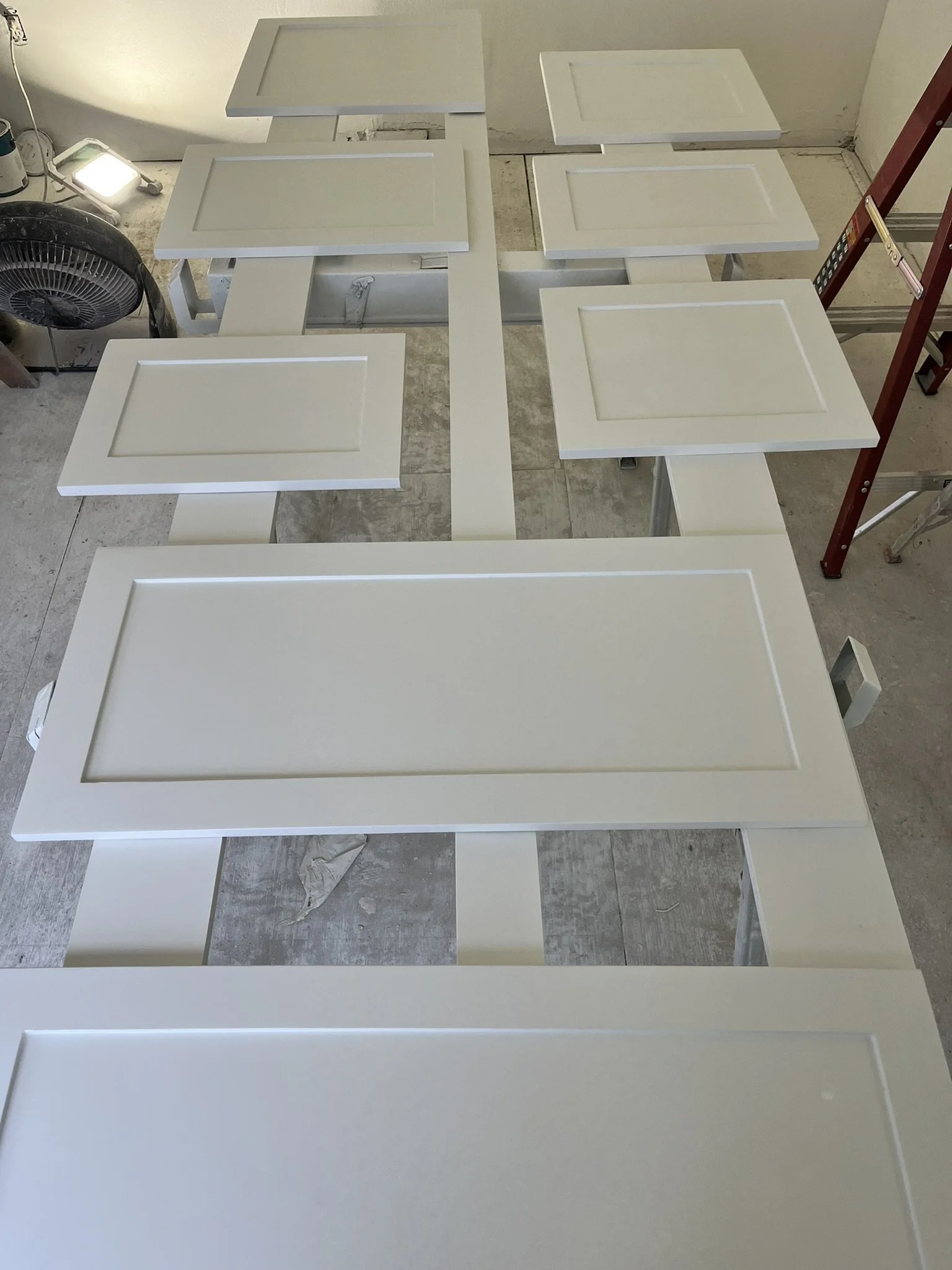 Several white cabinet doors laid out on a work table in a workshop.