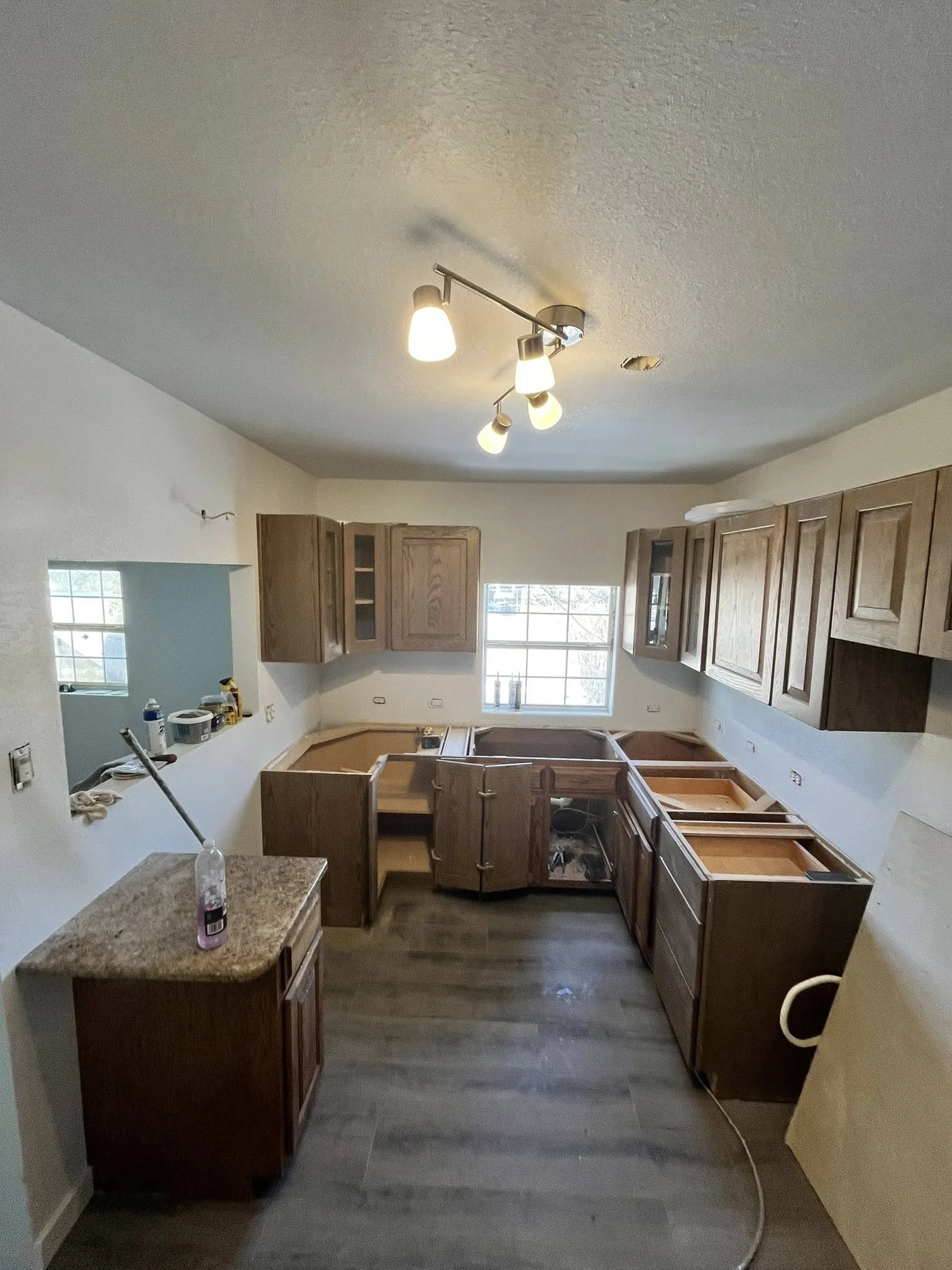 Unfinished kitchen with wooden cabinets, countertops, and flooring, no appliances installed, window providing natural light, ceiling light fixture turned on.