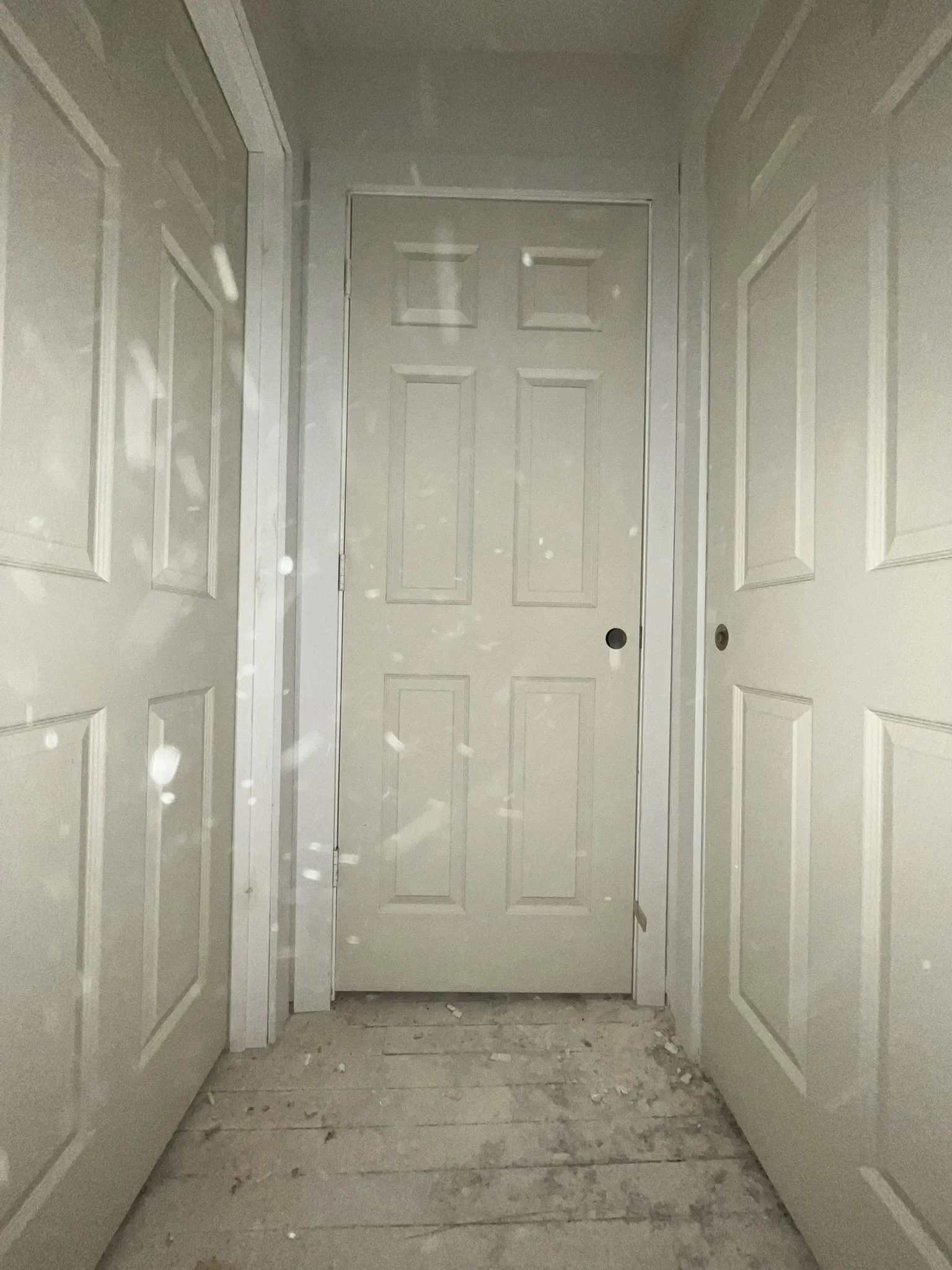 Interior hallway with three closed white doors, unfinished flooring with debris, and drywall walls.