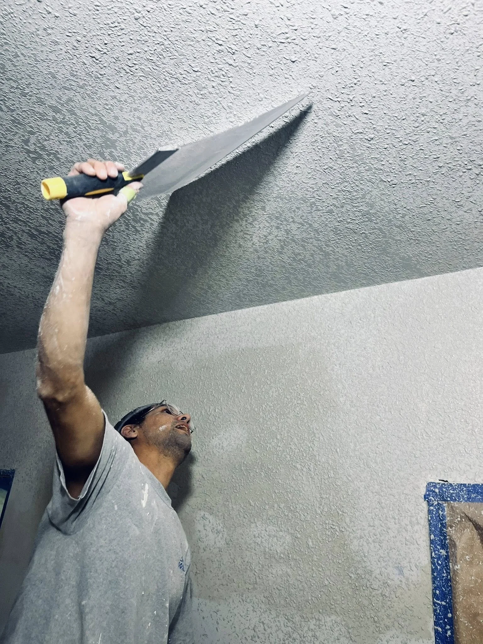 Person applying textured ceiling finish with a trowel on a ceiling.