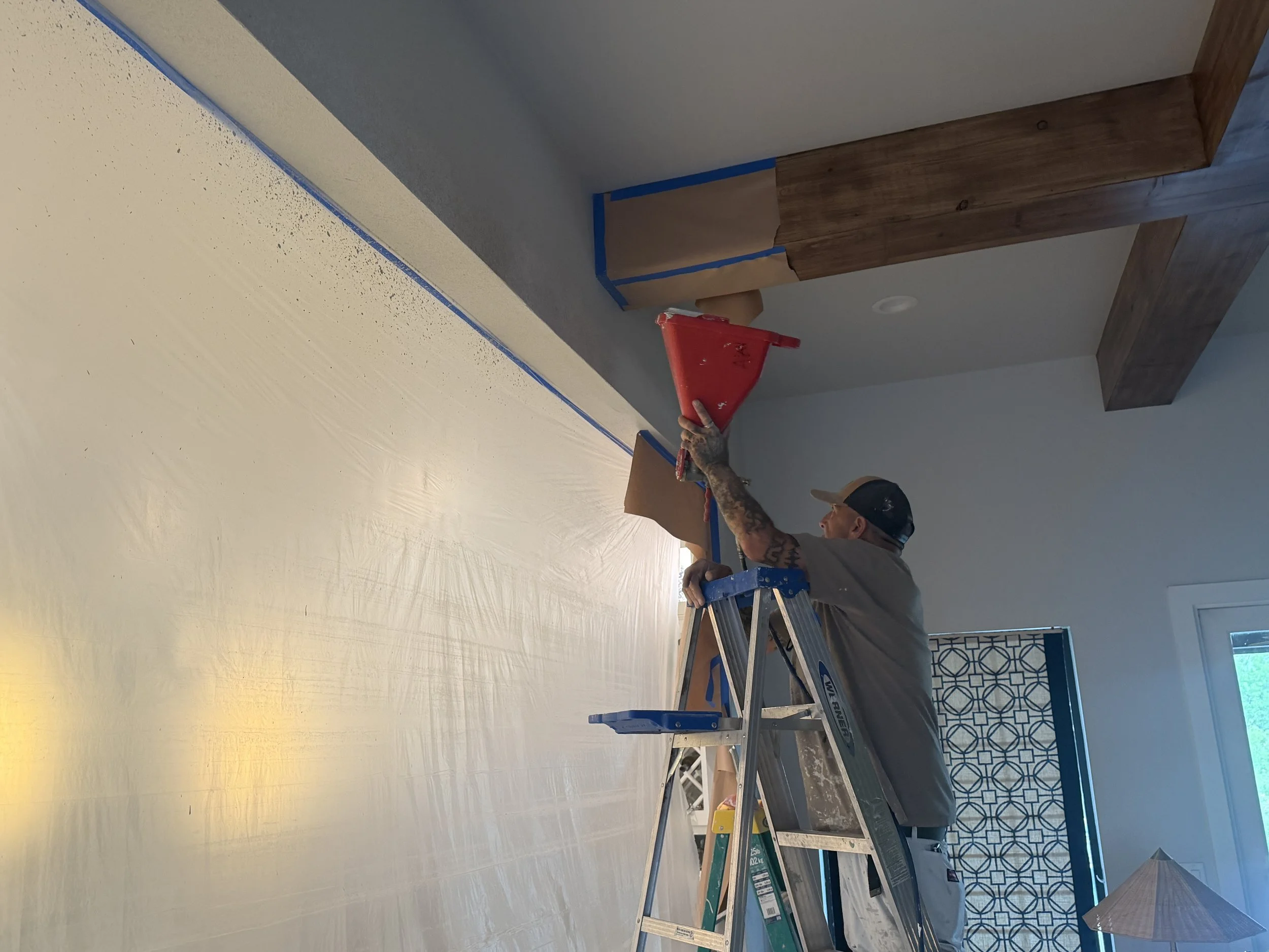 A person working on a home improvement project using a saw on a table, with a partially painted wall and taped edges.