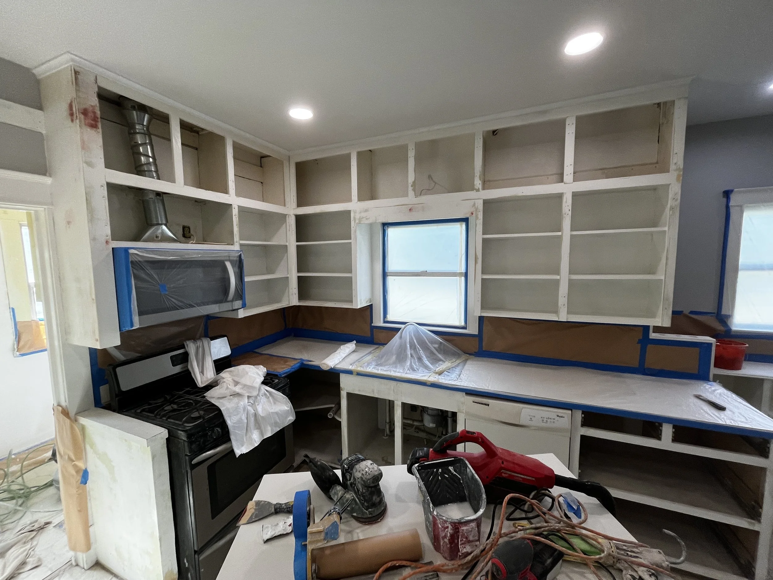 Kitchen undergoing renovation with unfinished cabinets, tools, and construction materials scattered around.