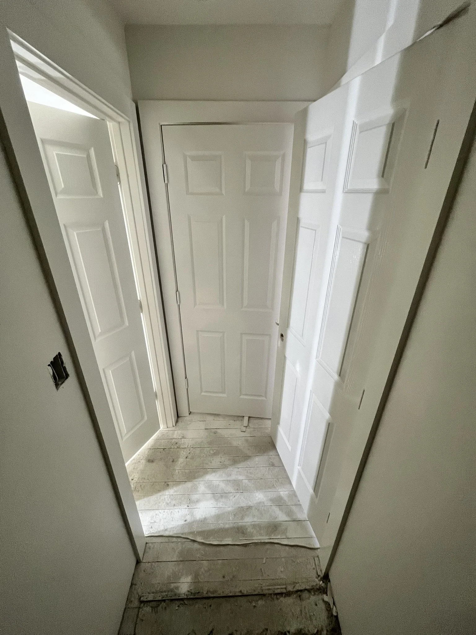 Small, unfinished interior space with white doors, some of which are partially open, and a light-colored wooden floor under construction.