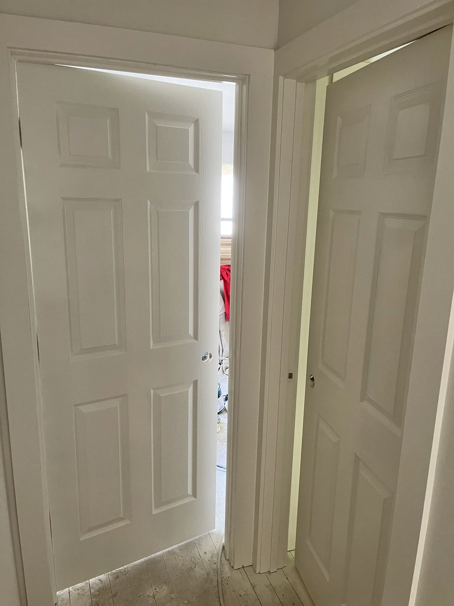 An interior view of a doorway with a partially open door leading to a room with a red jacket hanging and small items on the floor.
