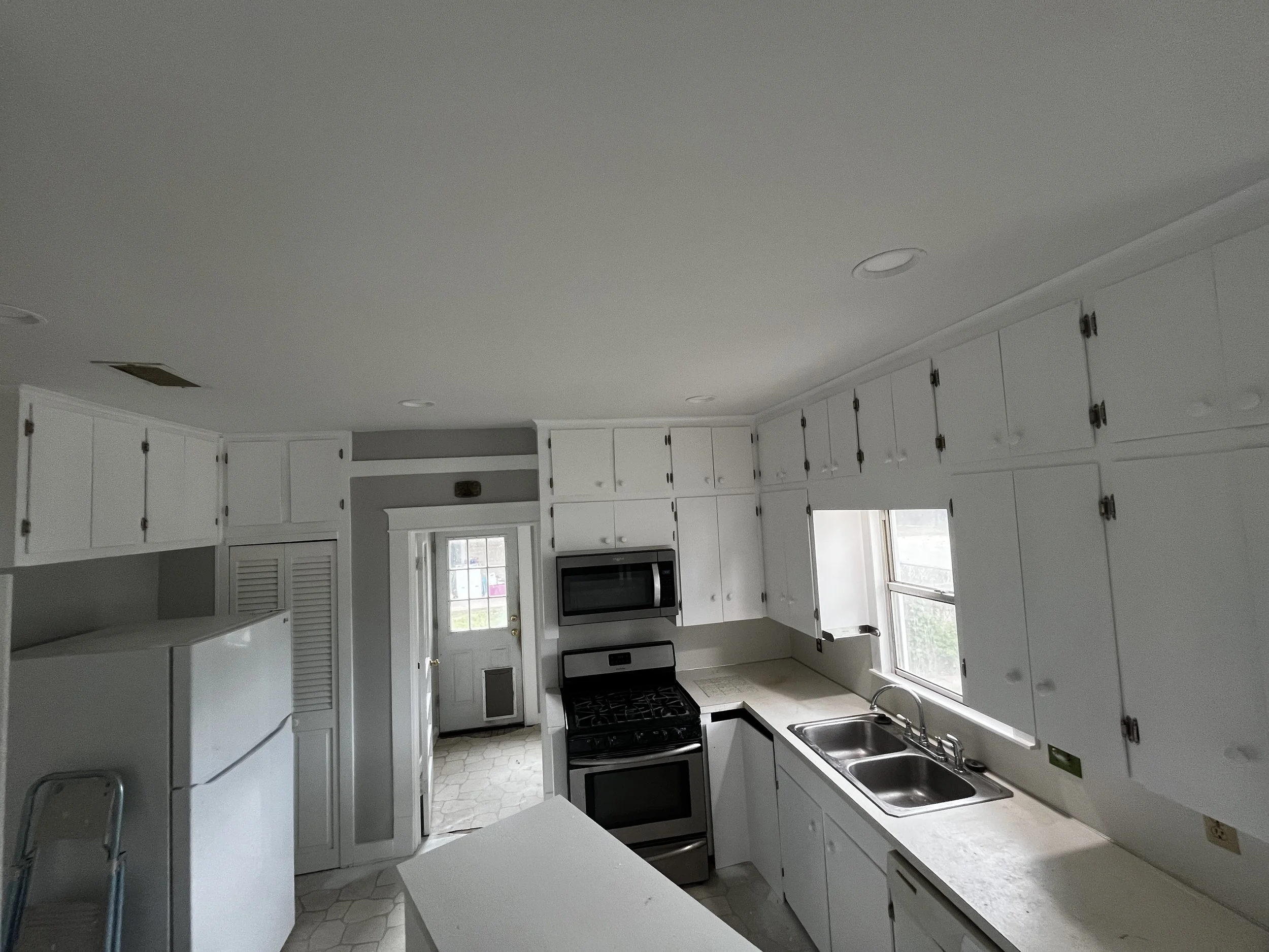 Kitchen with white cabinets, black appliances, a double sink, and windows letting in natural light.