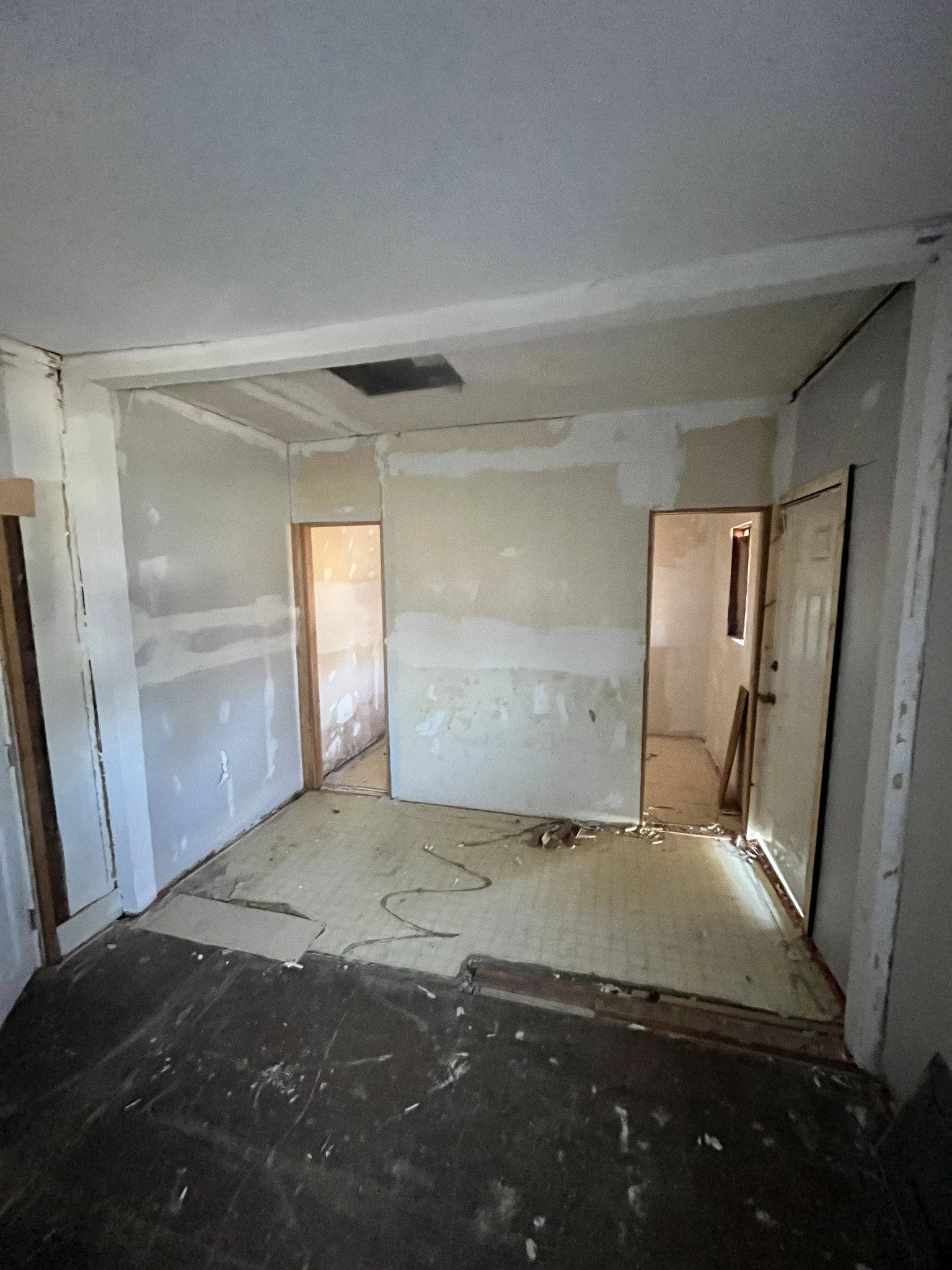 Interior of a room under renovation with drywall, exposed flooring, and construction materials.