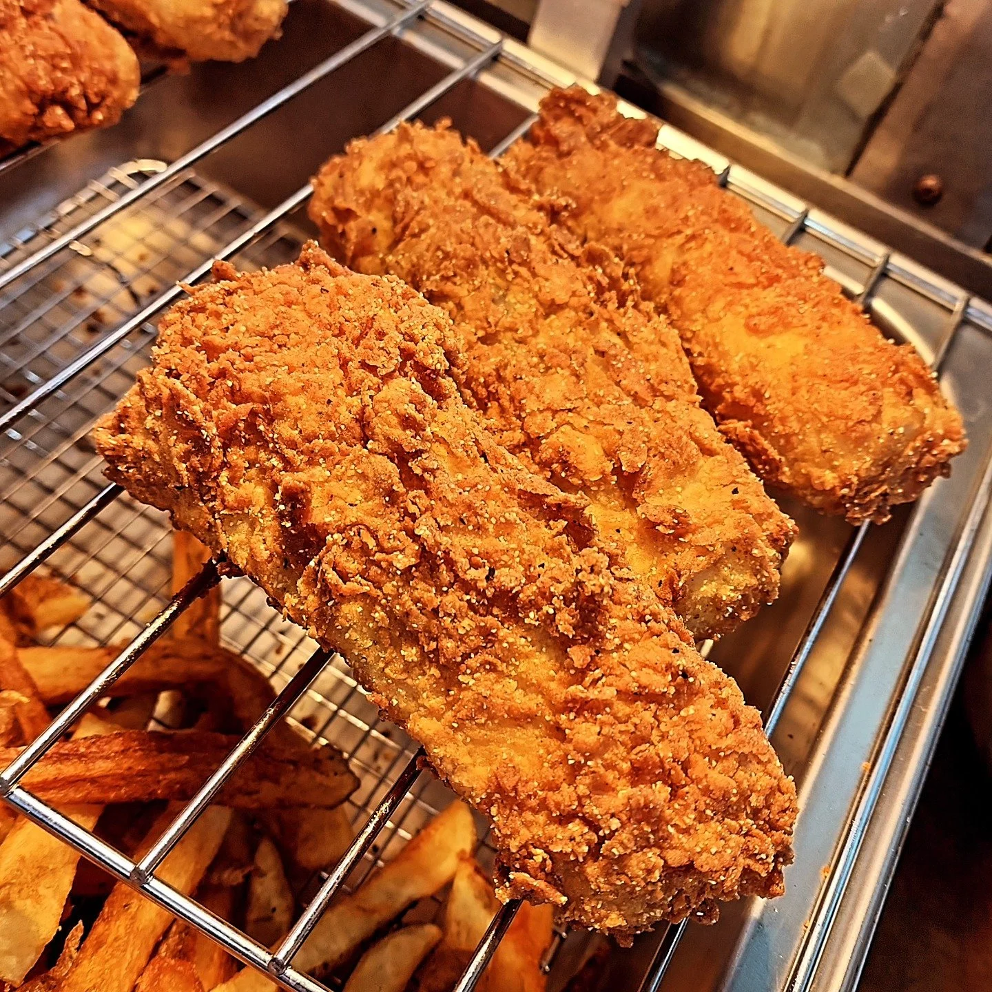 Close-up of three pieces of fried chicken with crispy, golden-brown coating on a metal wire rack.