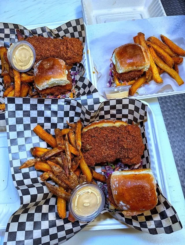 Three baskets of fried fish sandwiches with fries and dipping sauce on checkered paper.
