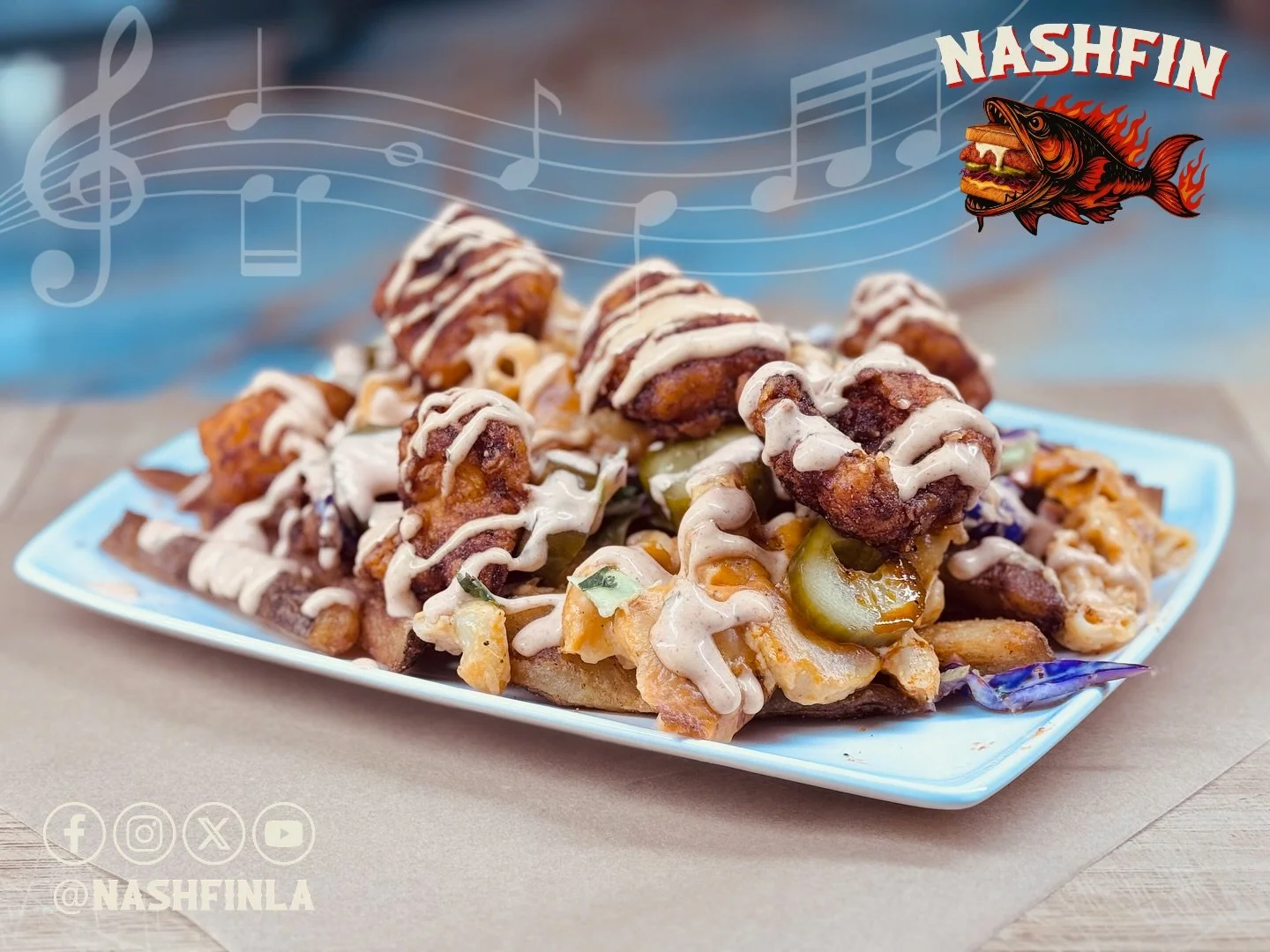 Plate of loaded fries topped with fried chicken pieces, drizzled with creamy sauce, and garnished with pickles.