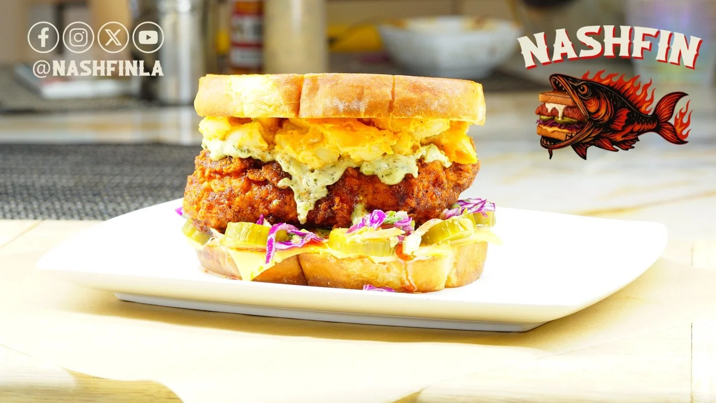 A plate with an everything bagel sandwich containing fried chicken, scrambled eggs, pickles, and purple cabbage, with a logo of a fish with flames and the text 'Nashfin' in the top right corner.