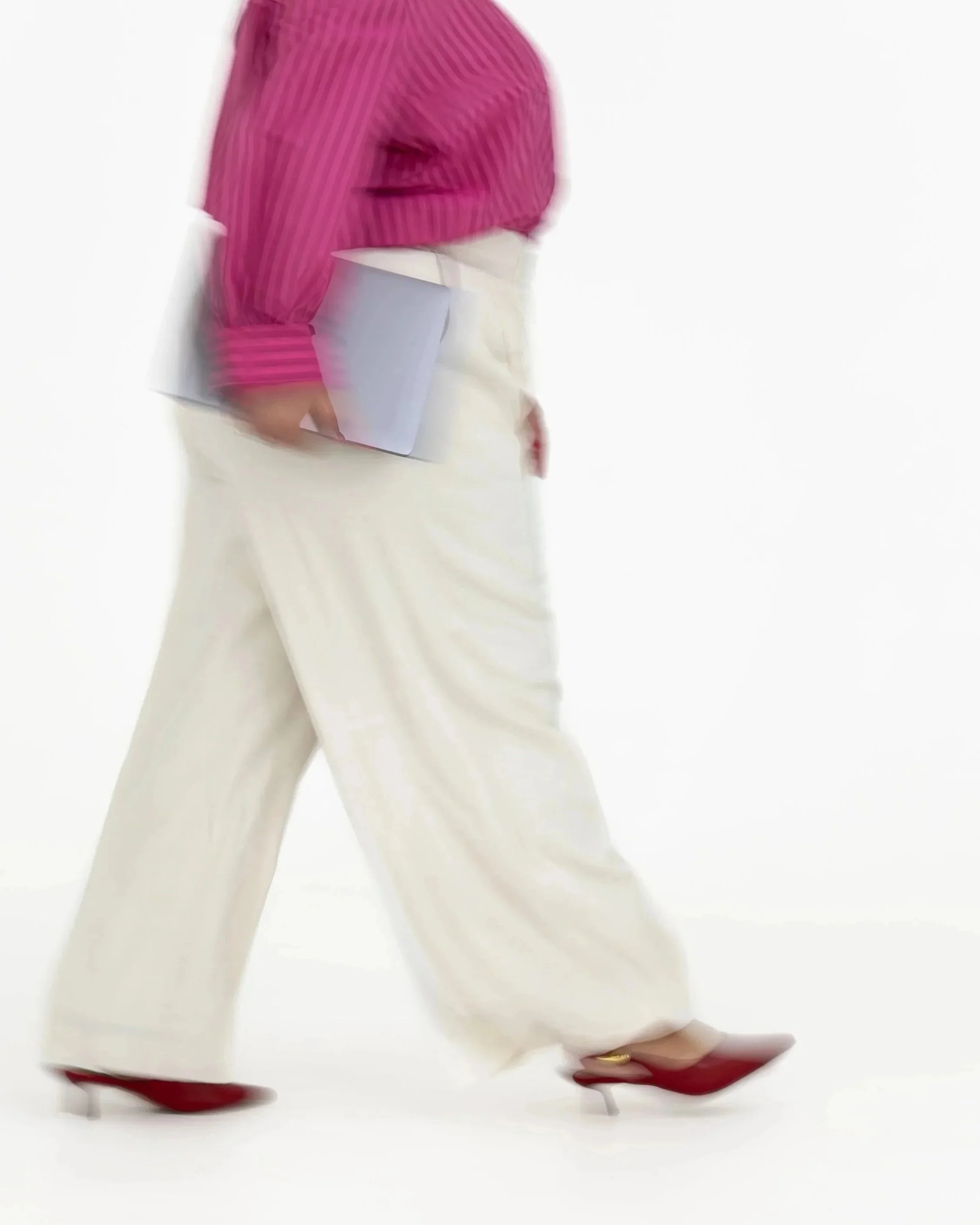 Close-up of a woman wearing pink striped blouse, white skirt, standing on red high heels, holding a gray card, against a plain white background.