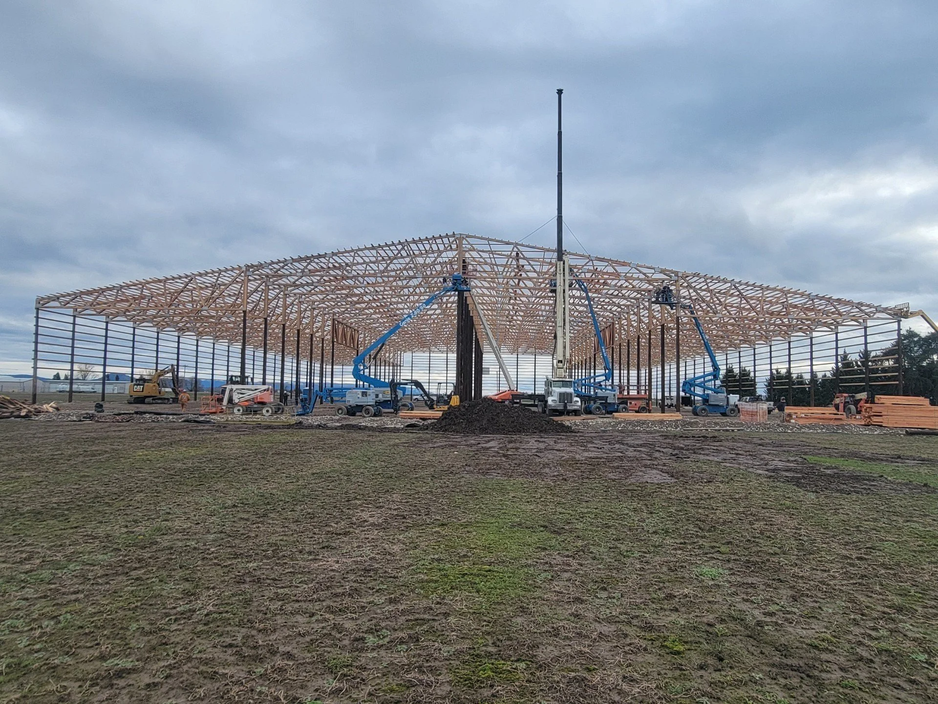 Construction site with partially built wooden roof structure and heavy machinery under overcast sky.