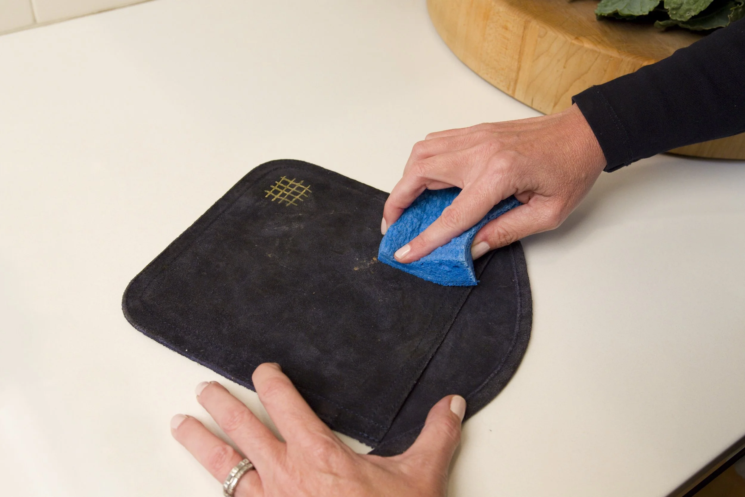 Person cleaning a suede oven mitt with a blue sponge.