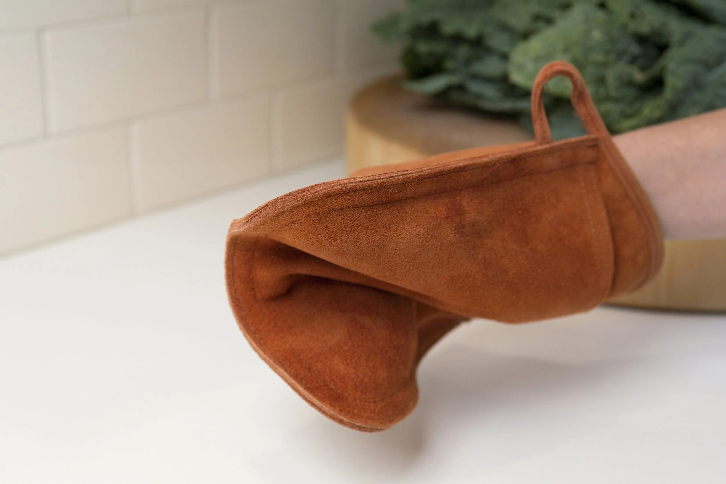 Close-up of a person's hand holding an orange cloth bag with a handle, with a green plant in the background.