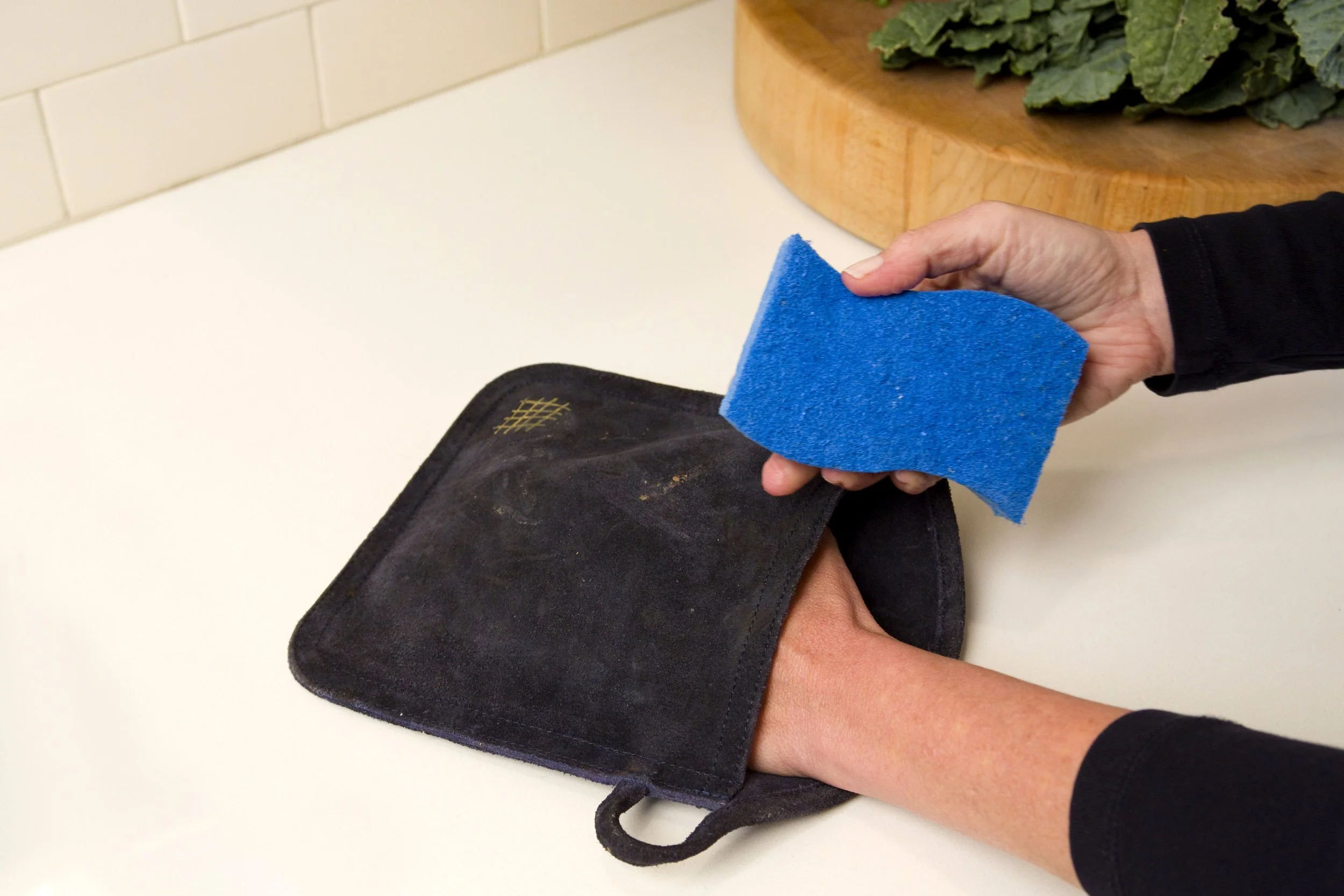 Person cleaning a suede oven mitt shoe with a blue sponge.
