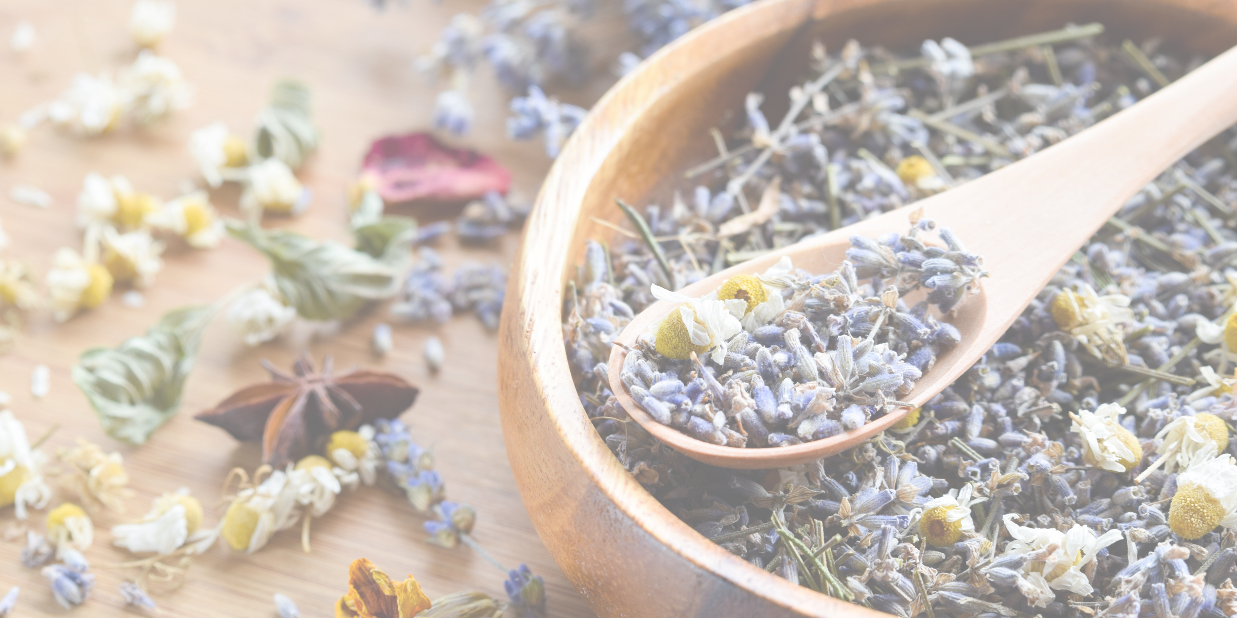 Dried lavender and chamomile in a wooden bowl with a wooden spoon on a wooden surface.