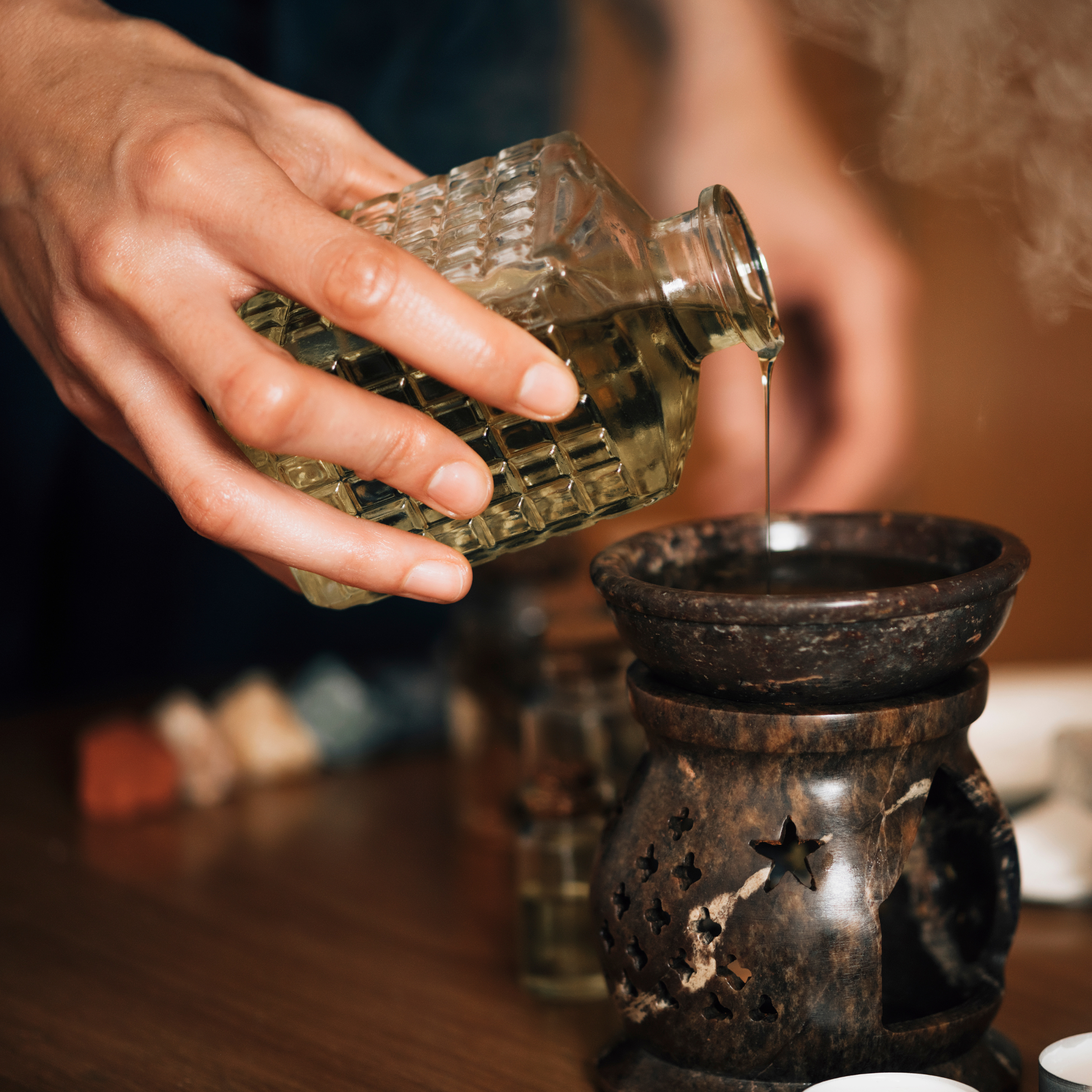 Person pouring essential oil from a glass bottle into an incense burner.