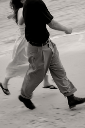 Close-up of two people tango dancing on a sandy beach, focusing on their lower bodies and legs.