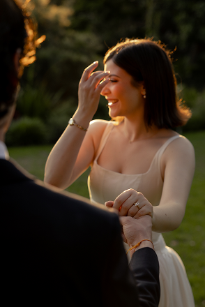A woman in a white dress smiling and laughing while holding hands with someone outdoors during sunset.