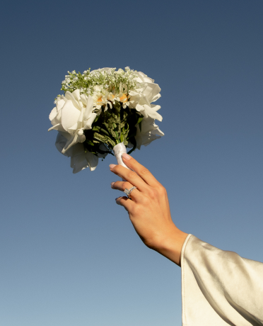 A person's hand holding a bouquet of white flowers against a clear blue sky